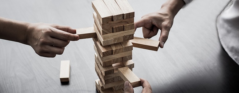 Stacked wooden blocks with pieces being removed, showing how a structure’s stability depends on its foundation.