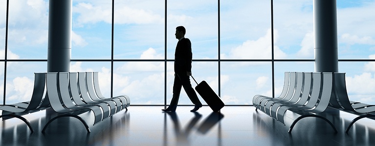 Traveller with luggage walking through an airport terminal as a plane takes off, representing modern cross‑border living and international spending